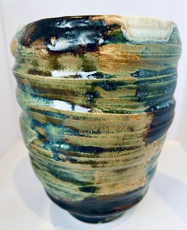 A textured ceramic vase in earthy tones of green, blue, and brown.